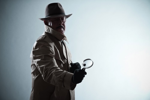 Silhouette of detective with mustache and hat. Holding magnifying glass. Studio shot.